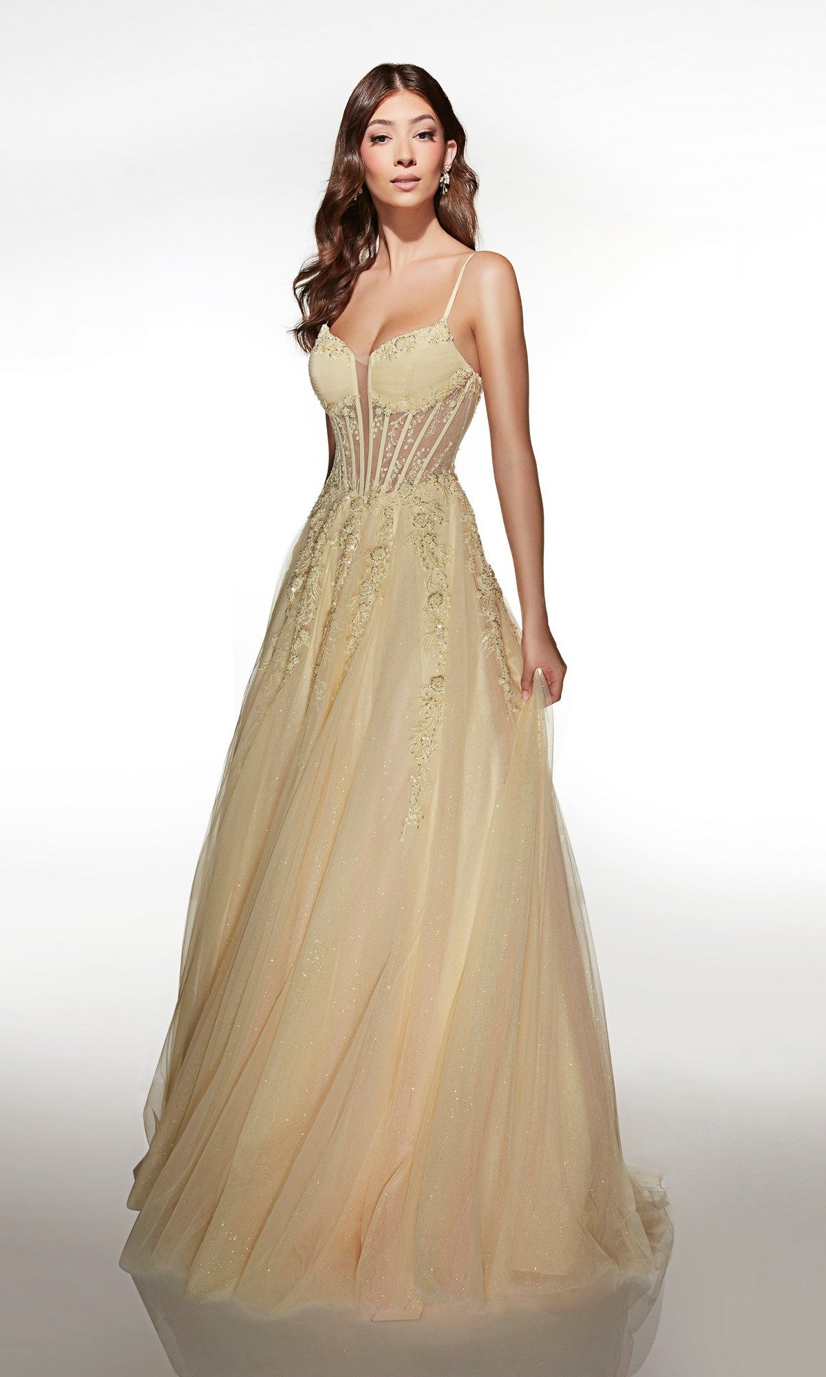 A woman wearing the Alyce 62061 long prom dress, a light yellow, floor-length gown featuring a fitted semi-sheer lace corset bodice, floral embroidery, and thin straps.